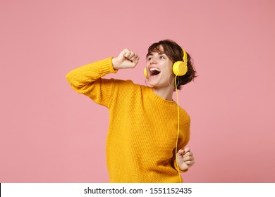 Funny Young Brunette Woman Girl In Yellow Sweater Posing Isolated On Pastel Pink Wall Background Studio Portait. People Lifestyle Concept. Mock Up Copy Space. Listen Music With Headphones, Sing Song