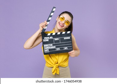 Funny Young Brunette Woman Girl In Yellow Casual Shirt Posing Isolated On Violet Wall Background In Studio. People Lifestyle Concept. Mock Up Copy Space. Hold Classic Black Film Making Clapperboard