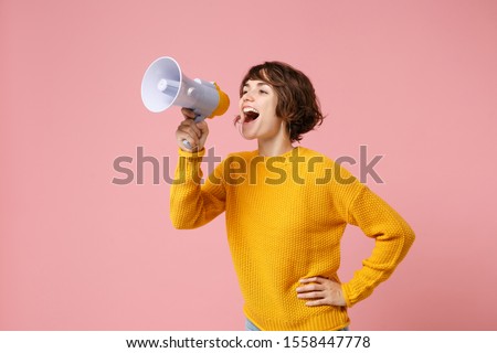 Funny young brunette woman girl in yellow sweater posing isolated on pastel pink wall background studio portrait. People sincere emotions lifestyle concept. Mock up copy space. Screaming in megaphone