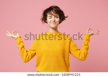 Funny young brunette woman girl in yellow sweater posing isolated on pastel pink background. People lifestyle concept. Mock up copy space. Hold hands in yoga gesture relaxing meditating looking aside