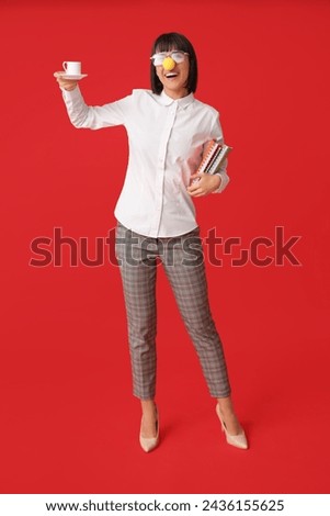 Funny young businesswoman with cup of coffee on red background. Fool's day