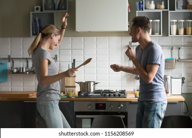 Funny young couple dancing to music together enjoying cooking in the kitchen, man and woman in love having fun preparing breakfast food feeling happy and carefree on weekend lifestyle at home