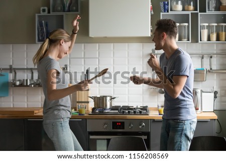 Funny young couple dancing to music together enjoying cooking in the kitchen, man and woman in love having fun preparing breakfast food feeling happy and carefree on weekend lifestyle at home