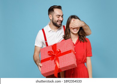 Funny young couple friends man woman in white red clothes hold present box with gift ribbon bow cover eyes with hand isolated on blue background. Valentine's Day Women's Day birthday holiday concept
