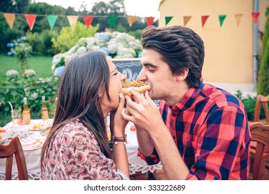 Funny young couple laughing and eating an american hot dog in a outdoors summer party