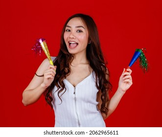 Funny young and cure Asian girl holding and playing party popers with funny and happy. Studio shot on red background.