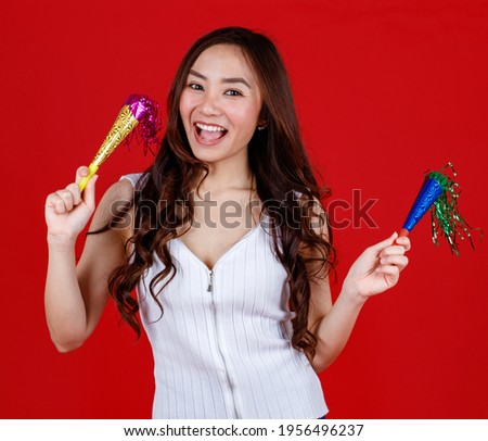 Funny young and cure Asian girl holding and playing party popers with funny and happy. Studio shot on red background.