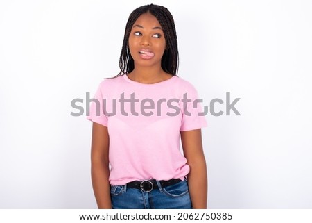 Funny Young girl with dreadlocks wearing pink t-shirt on white backgrond makes grimace and crosses eyes plays fool has fun alone sticks out tongue.
