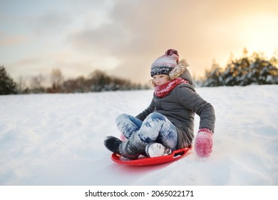 Funny young girl having fun with a sleigh in beautiful winter park. Cute child playing in a snow. Winter activities for kids.
