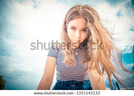 Funny young girl with long hair shows tongue against the blue summer sky