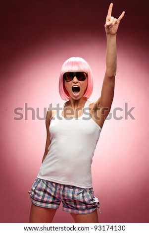 Funny young girl in pink wig and glasses dancing for camera across pink background