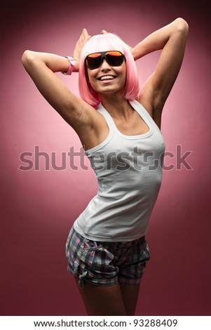 Funny young girl in pink wig posing for camera across pink background
