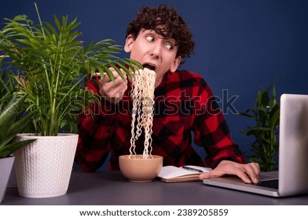 A funny young guy eats noodles during his lunch break. Office work.