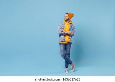 Funny young hipster guy in fashion jeans denim clothes posing isolated on pastel blue background studio portrait. People lifestyle concept. Mock up copy space. Holding hands crossed, looking aside