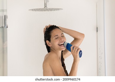 Funny young hispanic female singing aloud while showering holding gel shampoo bottle as microphone feel relaxed stress free. Joyful millennial woman in good mood having fun enjoy song in shower cabin
