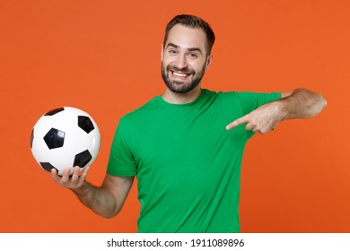 Funny Young Man Football Fan Point Index Finger On Green T-shirt Cheer Up Support Favorite Team With Soccer Ball Isolated On Orange Background Studio Portrait. People Sport Leisure Lifestyle Concept