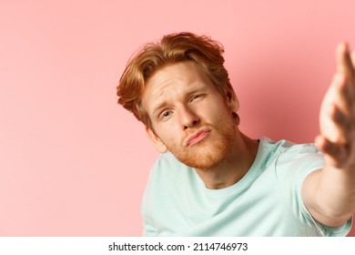 Funny Young Man With Red Messy Hair Taking Selife With Puckered Lips And Macho Expression, View From Smartphone Camera, Standing Over Pink Background