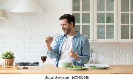 Funny Young Man Singing Song Into Whisk, Cooking In Modern Kitchen, Happy Male Holding Kitchenware As Microphone, Listening To Music, Dancing, Doing Housework At Home, Preparing Breakfast