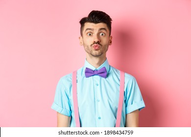 Funny Young Man Waiting For Kiss With Puckered Lips And Silly Face, Standing On Romantic Pink Background. Concept Of Love And Valentines Day