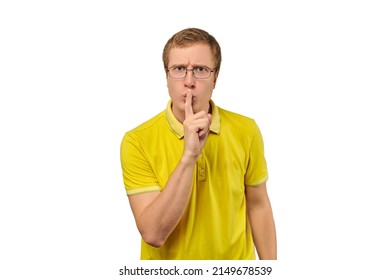 Funny young man in yellow T-shirt asking to be quiet, silence gesture isolated on white background. Young man in glasses saying Shhh, keep quiet, please and making silence gesture, request for silence