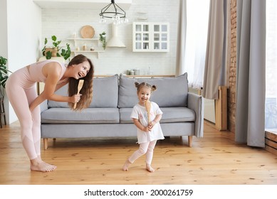 Funny young mom or nanny play sing entertain using kitchen appliances with little girl child. Happy family of two playing having fun singing favorite songs on kitchen together.