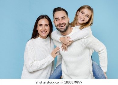 Funny young parents mom dad with child kid daughter teen girl in white sweaters giving piggyback ride to joyful, sitting on back isolated on blue background. Family day parenthood childhood concept - Shutterstock ID 1888379977