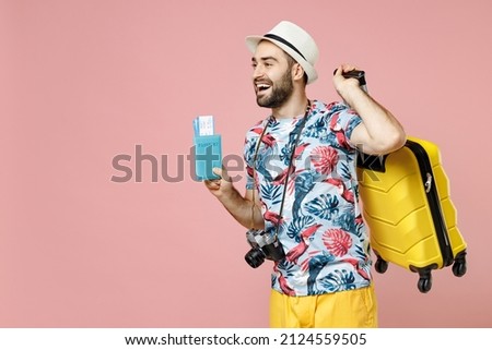 Funny young traveler tourist man in summer clothes hat photo camera hold suitcase passport ticket looking aside isolated on pink background. Passenger traveling on weekend. Air flight journey concept