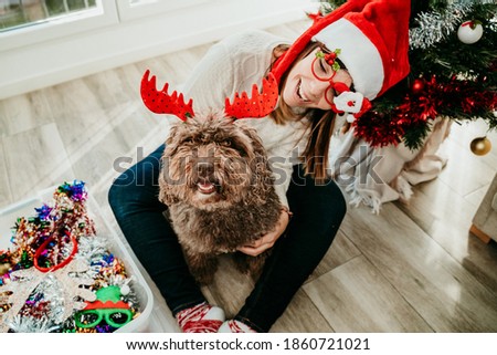 Funny young woman dressed up with christmas props playing with her cute spanish water dog at home. Christmas time