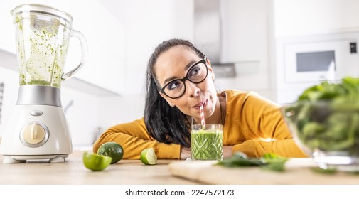 A funny young woman drinks a green smoothie that she made herself. - Powered by Shutterstock