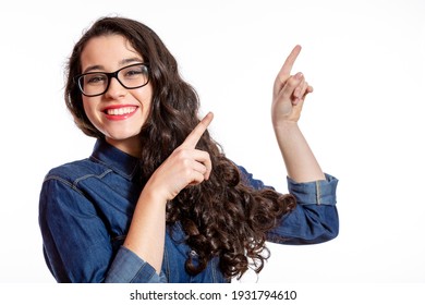 Funny young woman with glasses and denim shirt pointing with both hands at blank space. Isolated on white