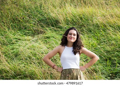 Funny Young Woman With Hands On Hips Biting A Grass Over A Grass Background