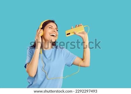 Funny young woman in headphones dance and sing listening to music on cellphone. Smiling overjoyed millennial girl isolated on blue studio background enjoy good quality sound in earphones.