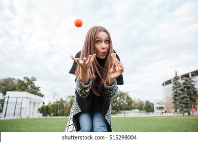 Funny Young Woman Holding Bone And Throwing Ball For Dog In Park