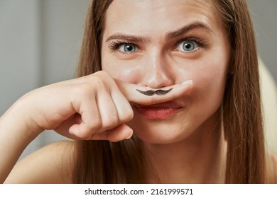a funny young woman holds a finger near her nose, on which a black mustache is drawn. hormones, unwanted hair removal