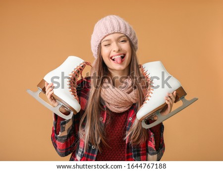 Funny young woman with ice skates on color background