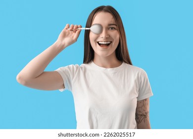 Funny young woman with silver spoon on blue background