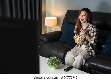 Funny Young Woman Watching TV And Eating Popcorn On Sofa At Night