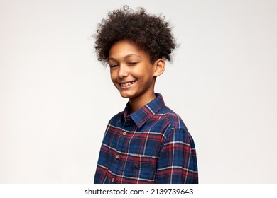 Funny-looking charismatic photogenic dark-skinned male kid with stylish afro haircut winking with smiling sly cunning face, wearing blue and red flannel shirt, standing against wall with copy space