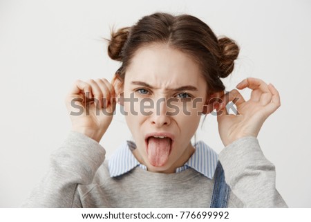 Funny-looking woman wearing casual grimacing with tongue out making ears protruding. Close up portrait of female troublemaker with trendy hairstyle being crazy fooling around. Joy concept