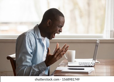 Furious African American Male Worker Look At Laptop Screen Screaming Experience Operational Gadget Problems, Angry Biracial Man Shout Yell Feel Stressed With Computer Spam, Breakdown Or Data Loss