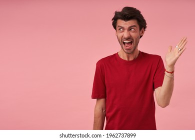 Furious aggressive young man with stubble in red tshirt arguing and screaming over pink background Looking to the side