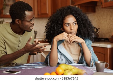 Furious black male gesturing in despair or anger while trying to make excuses to his offended wife as if saying: Can you just hear me out? African couple going through hard time in relationships