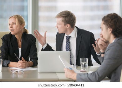 Furious Boss Scolding Young Frustrated Interns With Bad Work Results. Ineffective Office Workers Sitting At The Table And Listening To Irritated Boss Yelling With Bored And Annoyed Expressions
