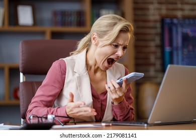 Furious Businesswoman Shouting Expressively To Smart Phone While Answering Phone Call At Office. Angry Annoyed Woman Enraged Of Bad Service, Having Problem With Not Working Mobile Phone, Get Spam