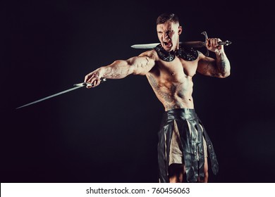 Furious muscular man posing shirtless with dangerous weapon and screaming in dark.