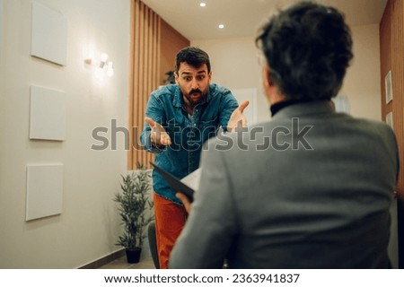 A furious patient is yelling and expressing anger at the doctor's office during his session with a shrink. A young angry man is yelling and expressing himself while having psychotherapy.