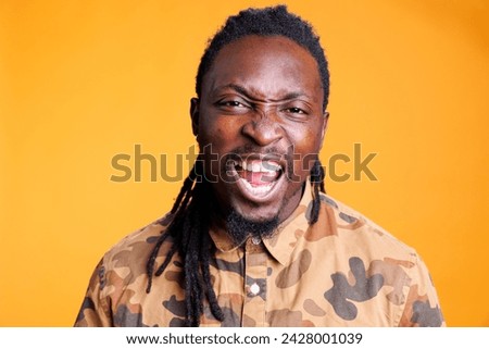Furious stressed man having breakdown while posing aggresive in studio over yellow background, showing unpleasant reaction. African american young adult feeling frustrated and mad
