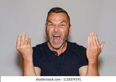 Furious vehement middle-aged man yelling at the camera gesturing with his hands in rage in a communication concept against a studio background - Shutterstock ID 1118379191