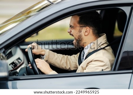 A furious young businessman is honking at other drivers in traffic. Road rage.