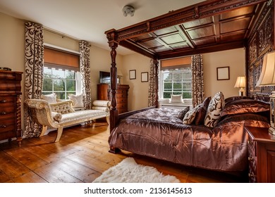 Furnished bedroom within former victorian rectory with ornate carved four poster bed and matching period sideboard drawers, chaise longe, side tables with lamps and exposed timber floor - Shutterstock ID 2136145613